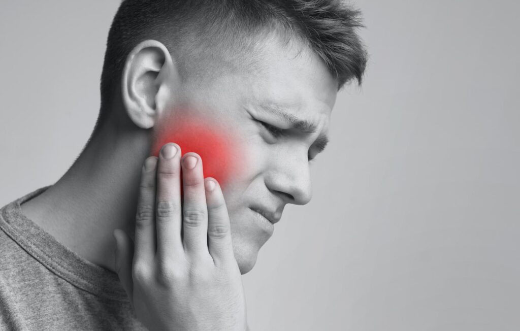 Dental problem. Young man suffering from strong toothache, monochrome photo with red inflamed zone, free space